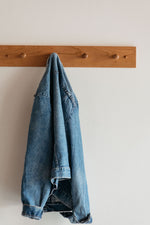 a blue jean jacket hung on a wooden peg rack on a white wall