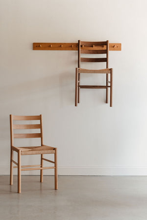 Knox ladder back chair hung on a Shaker peg rack with a second chair on the ground on a white wall 