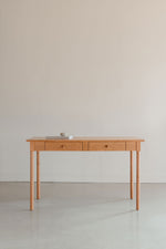 Writing desk in clean bright room with round legs and two drawers, and topped with a book and a rock