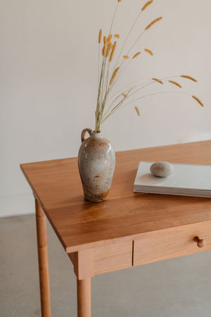 Vase with grasses, a book and a rock on the desktop of a cherry wood writing desk